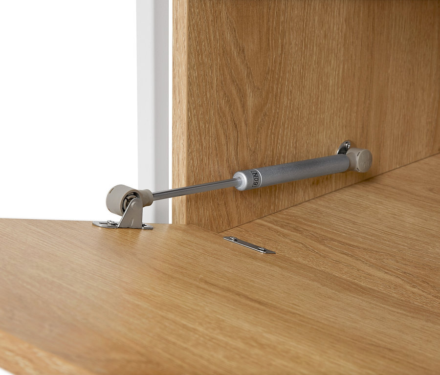 Detailansicht eines Möbelscharniers an einer hellbraunen Holzoberfläche.