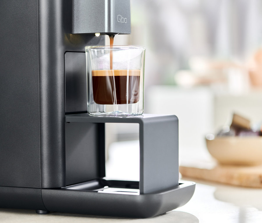 Kaffee wird aus einer Qbo ESSENTIAL Dark Stone Kaffeemaschine in ein Glas gegossen.
