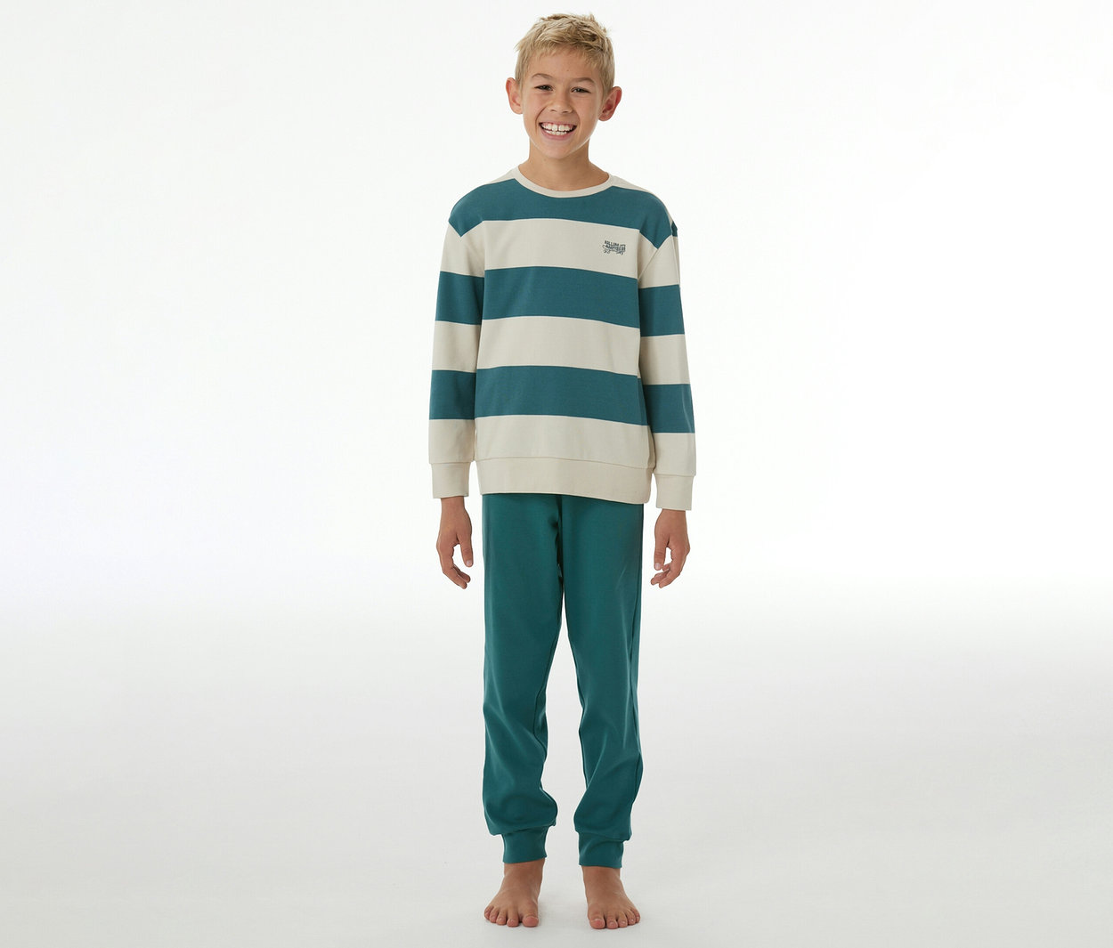 Lächelnder Junge in einem SCHIESSER Kinder-Interlock-Pyjama mit gestreiftem Oberteil in Petrol und Creme und petrolfarbener Hose.