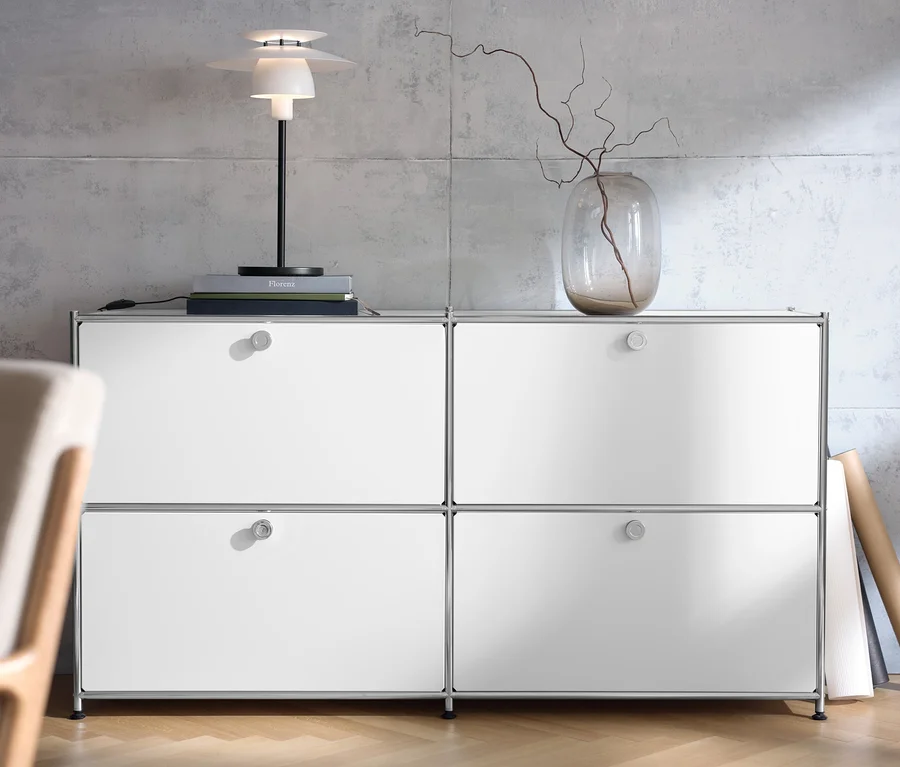 Weißes Sideboard »CN3« mit vier Klappen, darauf eine Tischleuchte aus Metall und eine Vase mit Zweigen.