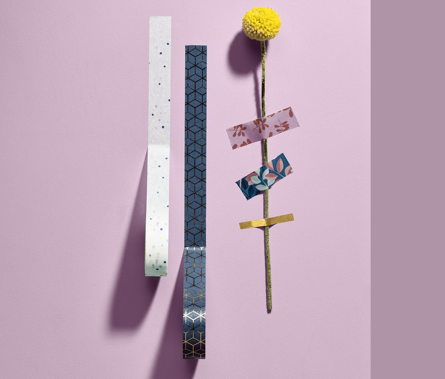 Zwei Rollen 10 Deko-Klebebänder und eine gelbe Blume mit Klebebändern am Stiel.