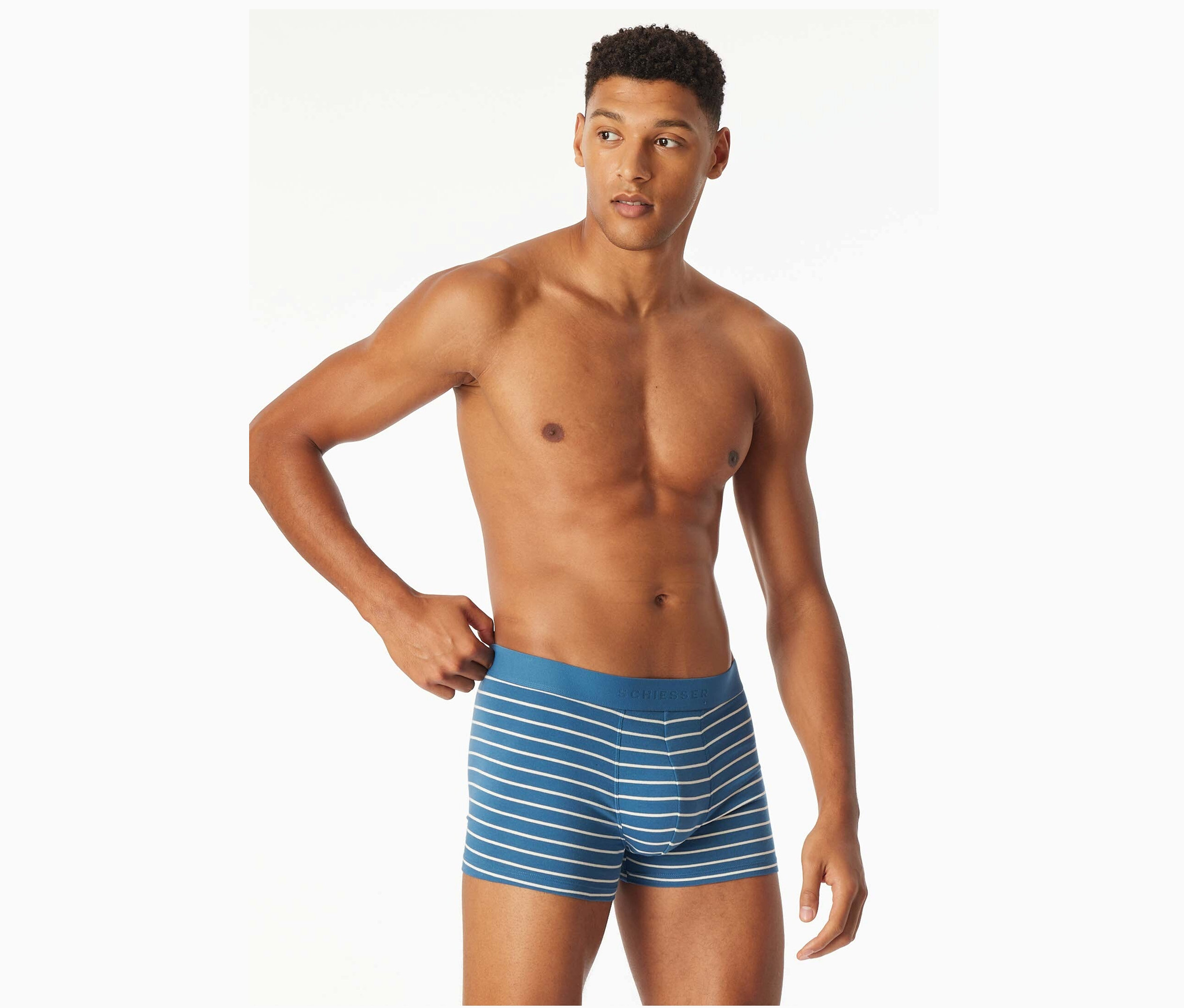 Mann mit freiem Oberkörper zupft an blauen Boxershorts mit weißen Streifen.