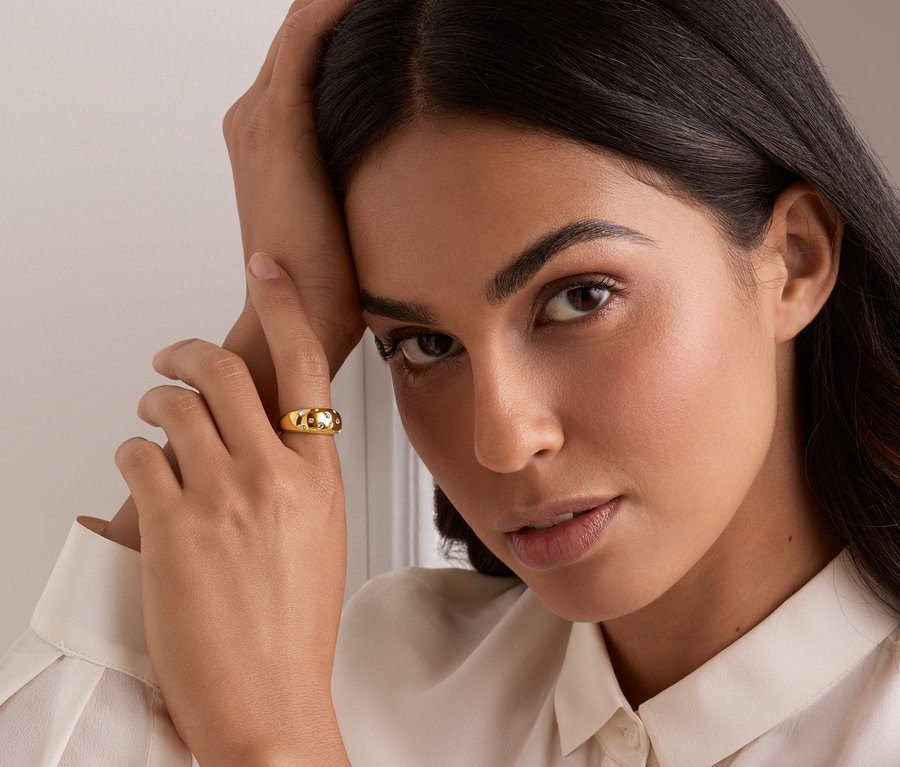 Frau stützt sich auf ihre Hand, am Finger ein goldener Ring mit Glaskristallen.