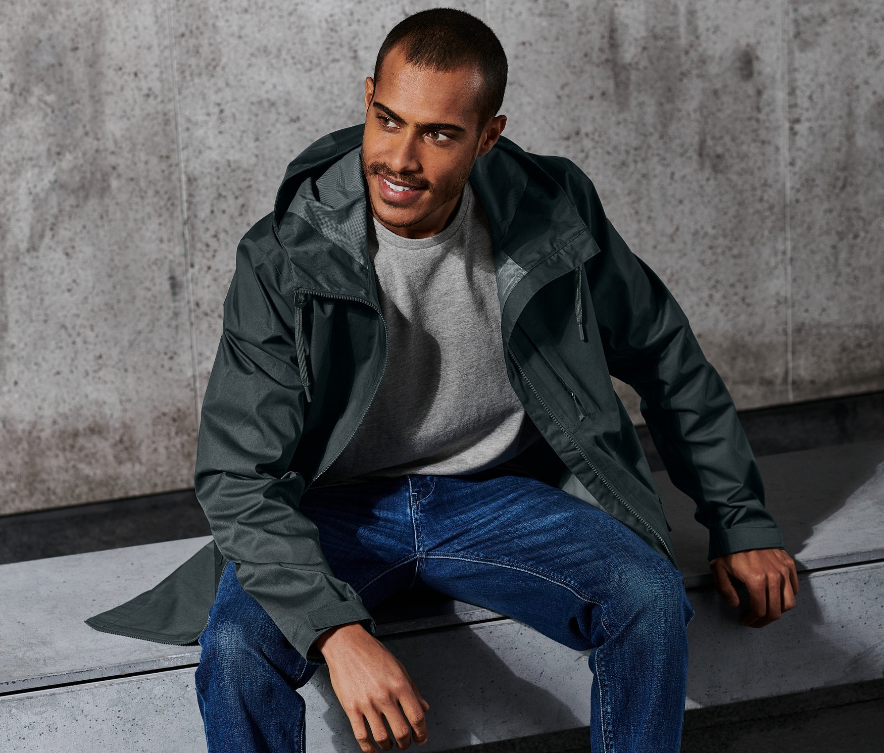 Mann sitzt in Outdoor-Jacke auf Bank.