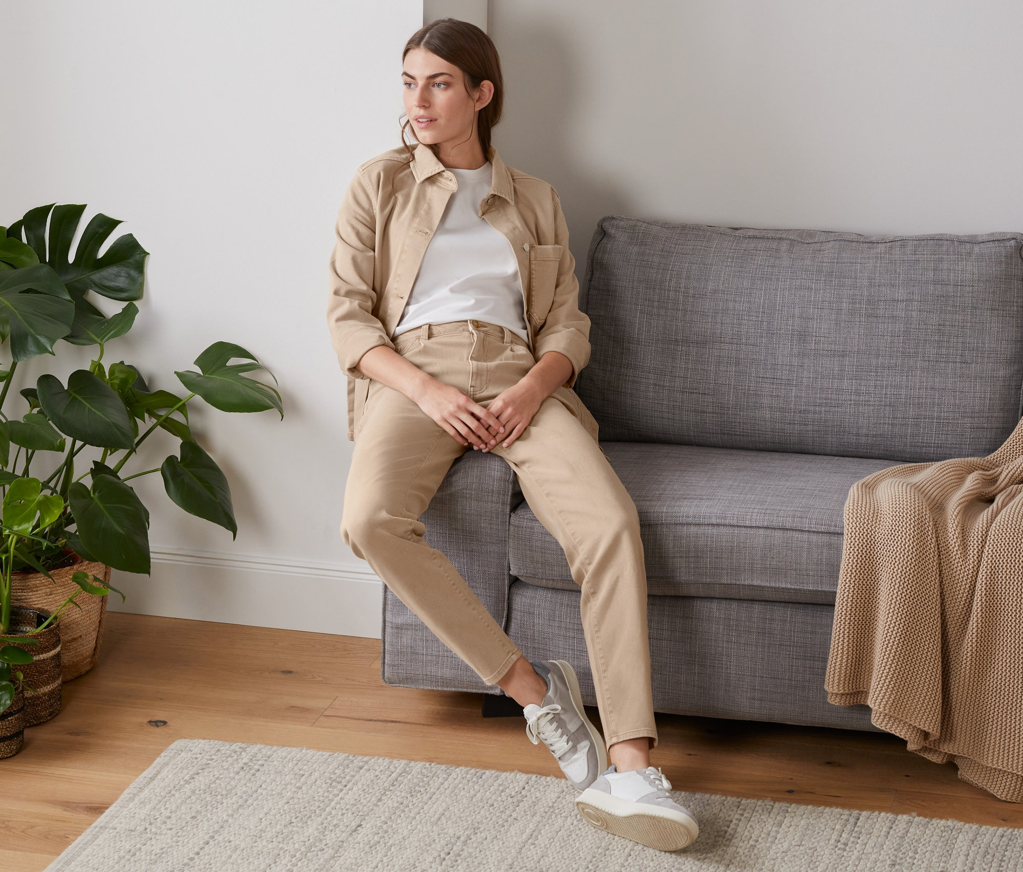 Frau sitzt auf einem grauen Sofa und trägt eine beige Girlfriend-Jeans.