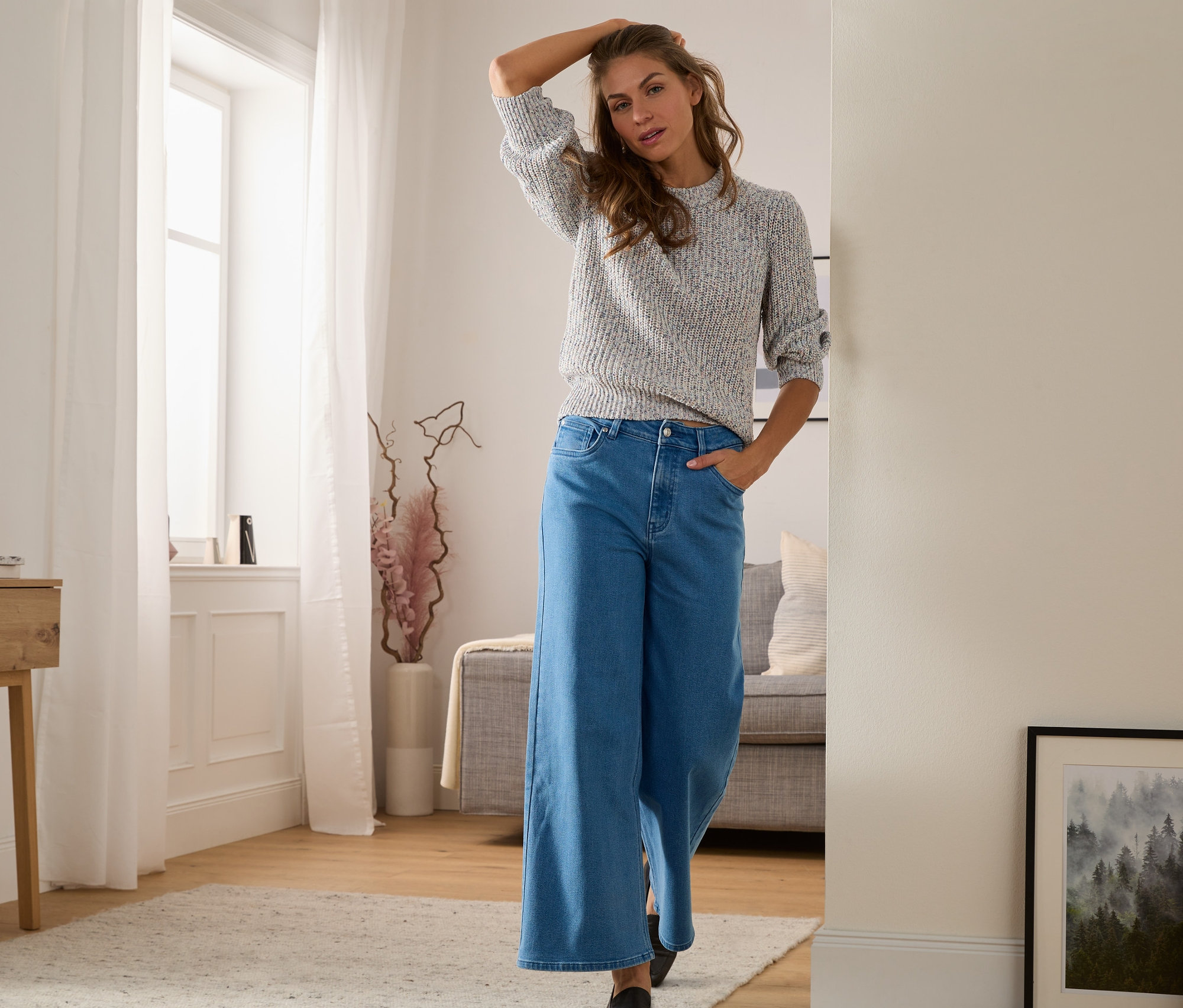 Frau posiert in einer Culotte-Jeans in Midblue-Denim und einem Pullover.
