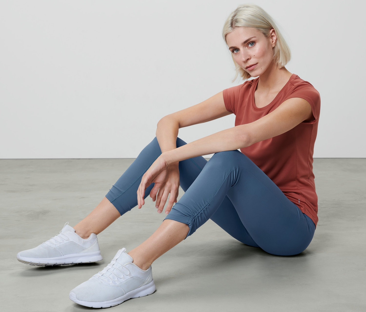 Frau sitzt in 7/8-Sporttight und T-Shirt auf dem Boden.