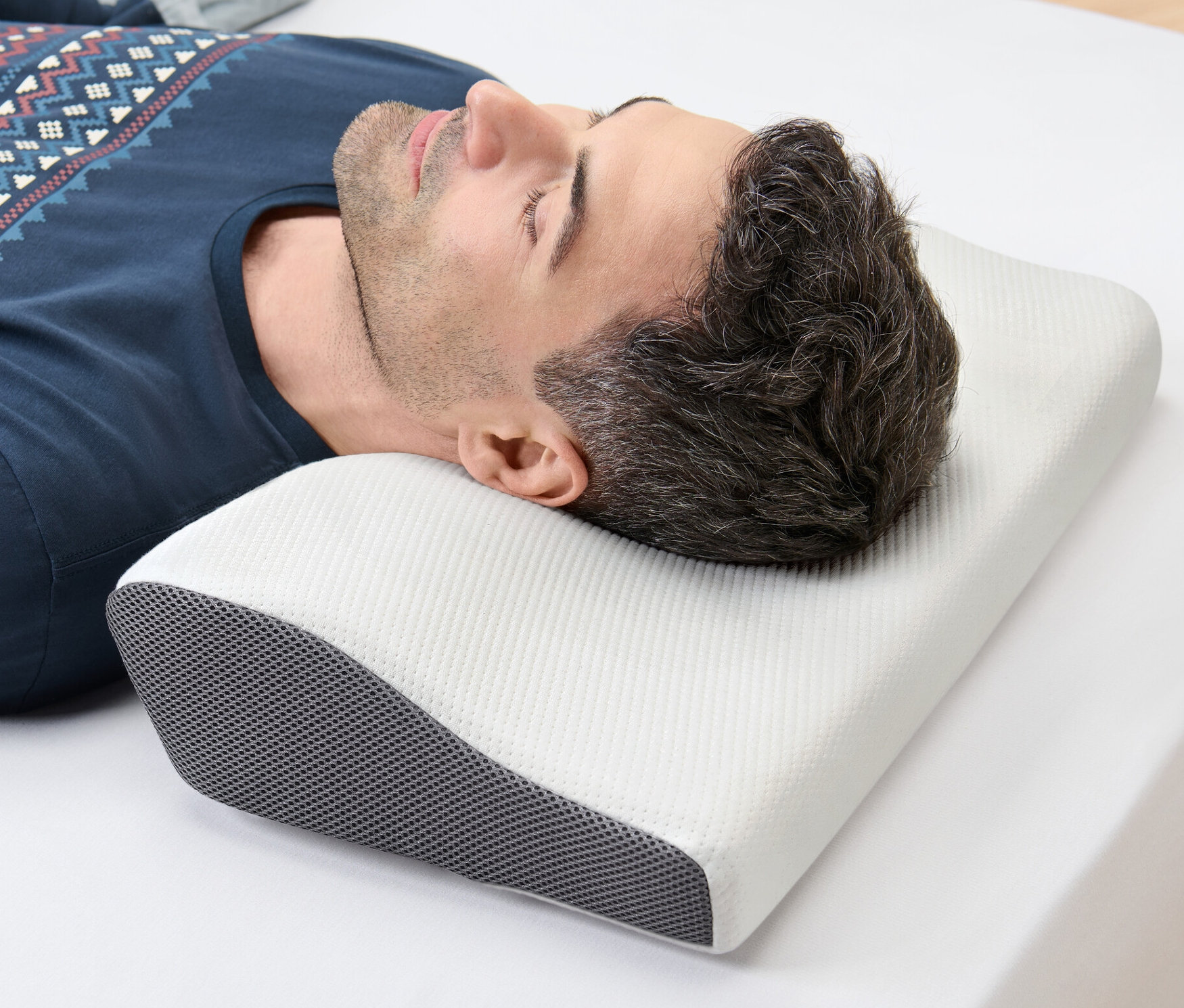 Mann liegt seitlich auf einem weißen Bettlaken und hat seinen Kopf auf einem Nackenstützkissen.