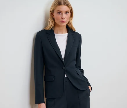 Blonde Frau posiert in einem marineblauen Jerseyblazer.