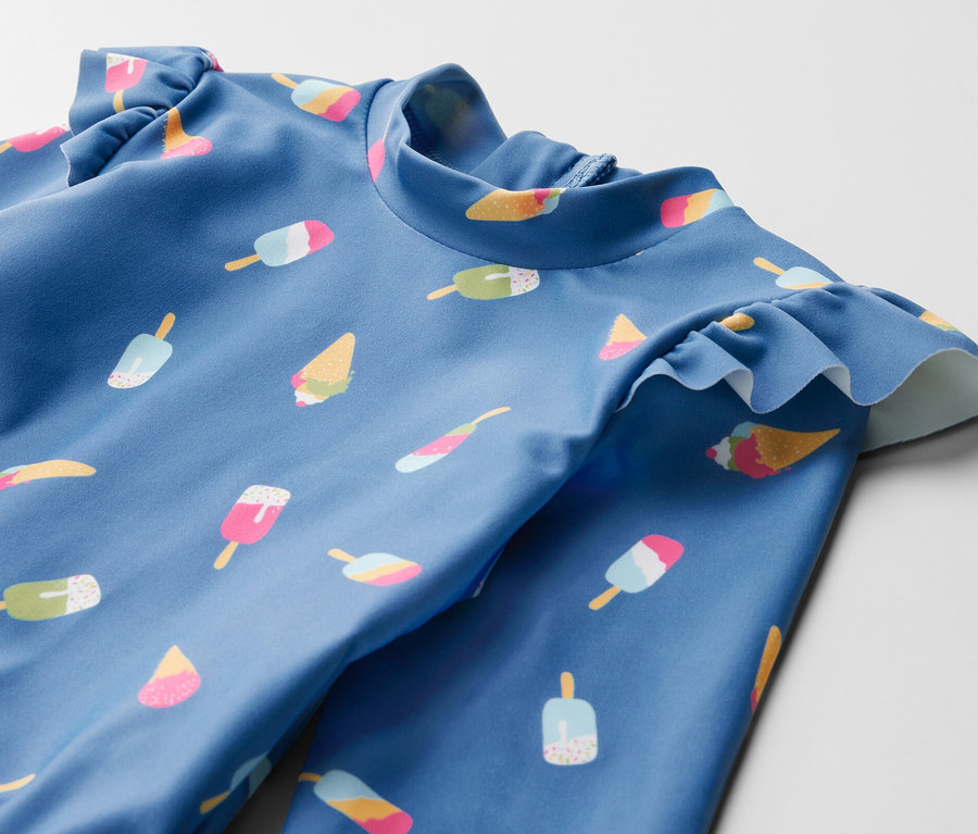 Detailaufnahme eines blauen Kinder-Badeanzugs mit Eiscreme-Print und UV-Schutzfaktor 80.