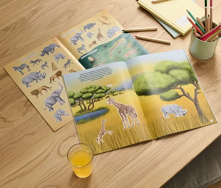 Offenes Stickerbuch "Faszierende Stickerwelt – wilde Tiere" mit Wildtiermotiven auf einem Holztisch.
