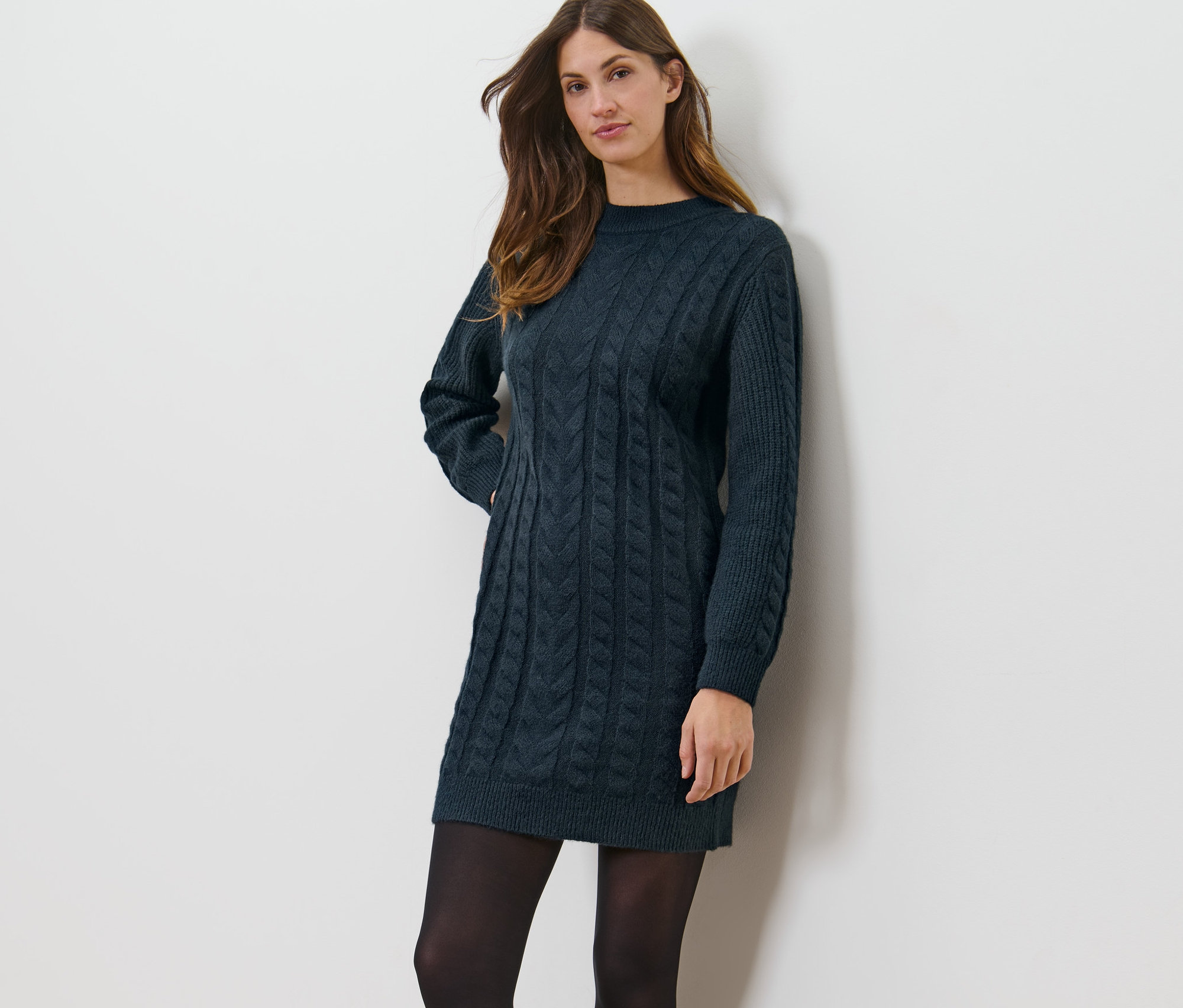 Frau posiert in einem Strickkleid mit Zopfmuster.