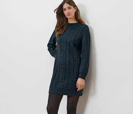 Frau posiert in einem Strickkleid mit Zopfmuster.