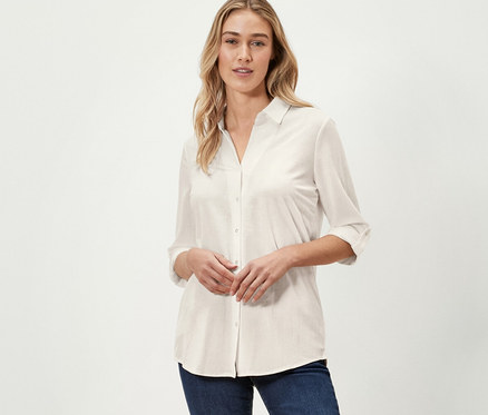 Frau posiert in cremeweißer Piqué-Jerseybluse und dunkelblauen Jeans.