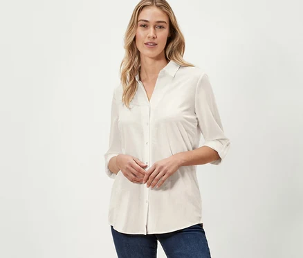 Frau posiert in cremeweißer Piqué-Jerseybluse und dunkelblauen Jeans.