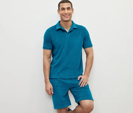 Mann posiert in einem petrolfarbenen Frottee-Poloshirt und Shorts.