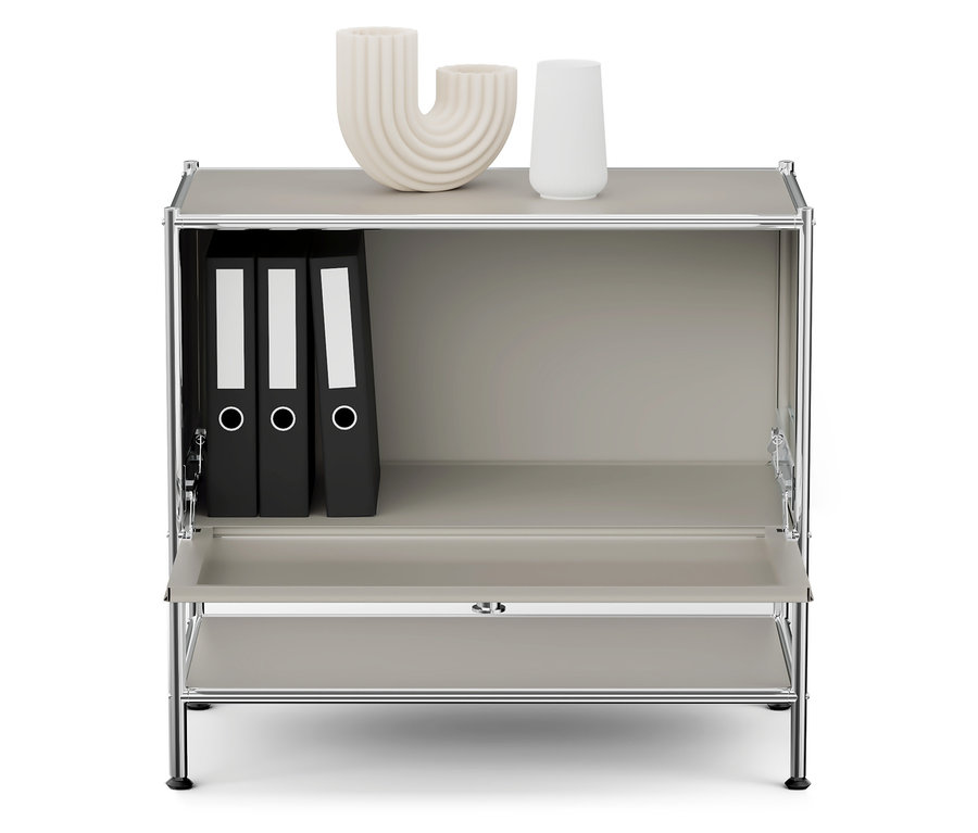 Grauer Schrank mit Chromrahmen, auf der oberen Ablage stehen zwei weiße Vasen und im oberen Fach drei schwarze Ordner.