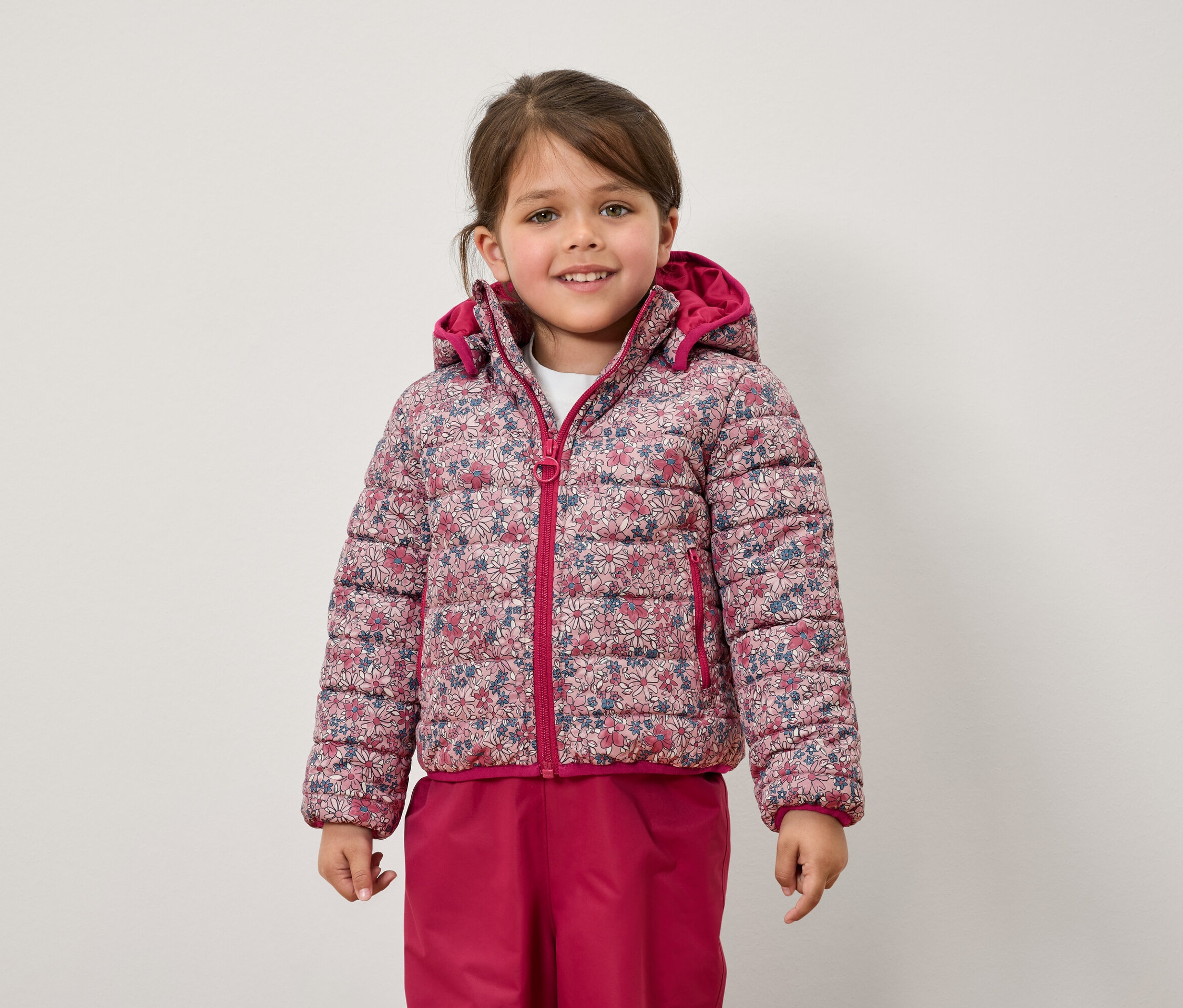 Ein Mädchen trägt eine geblümte Jacke und eine pinke Hose.