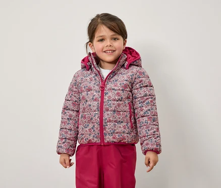 Ein Mädchen trägt eine geblümte Jacke und eine pinke Hose.
