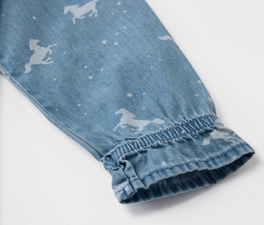 Detail eines Ärmels eines Kinder-Jeanskleids mit Pferde- und Sternenmuster.