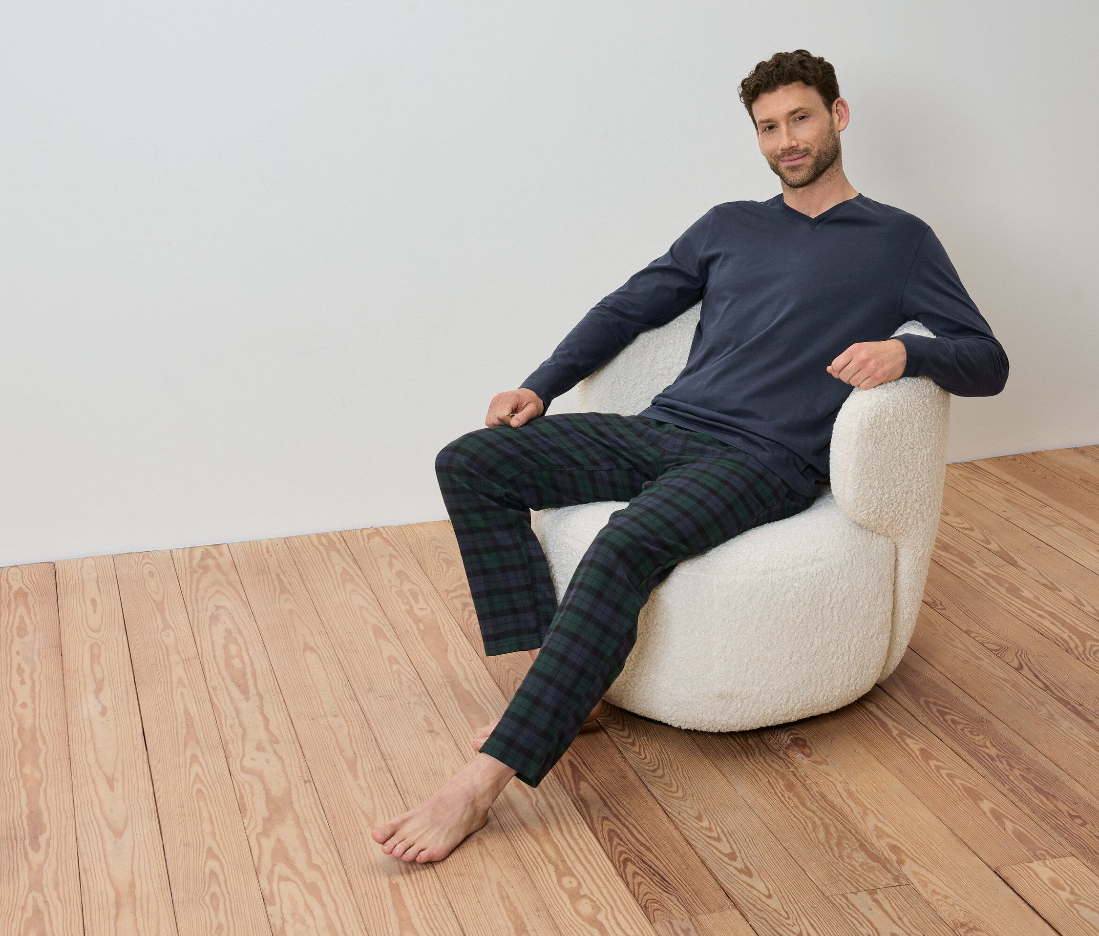 Mann sitzt in einem Sessel mit einem blauen Langarmshirt und einer karierten Hose.