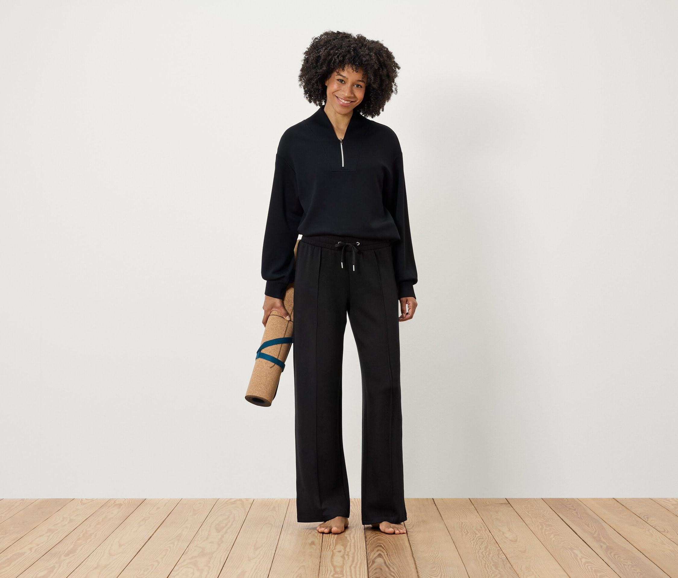 Frau hält Yogamatte in schwarzer Kleidung.