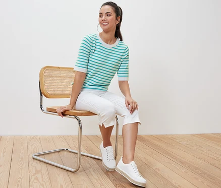 Frau sitzt auf einem Stuhl und trägt einen gestreiften Feinstrickpullover in Aqua.
