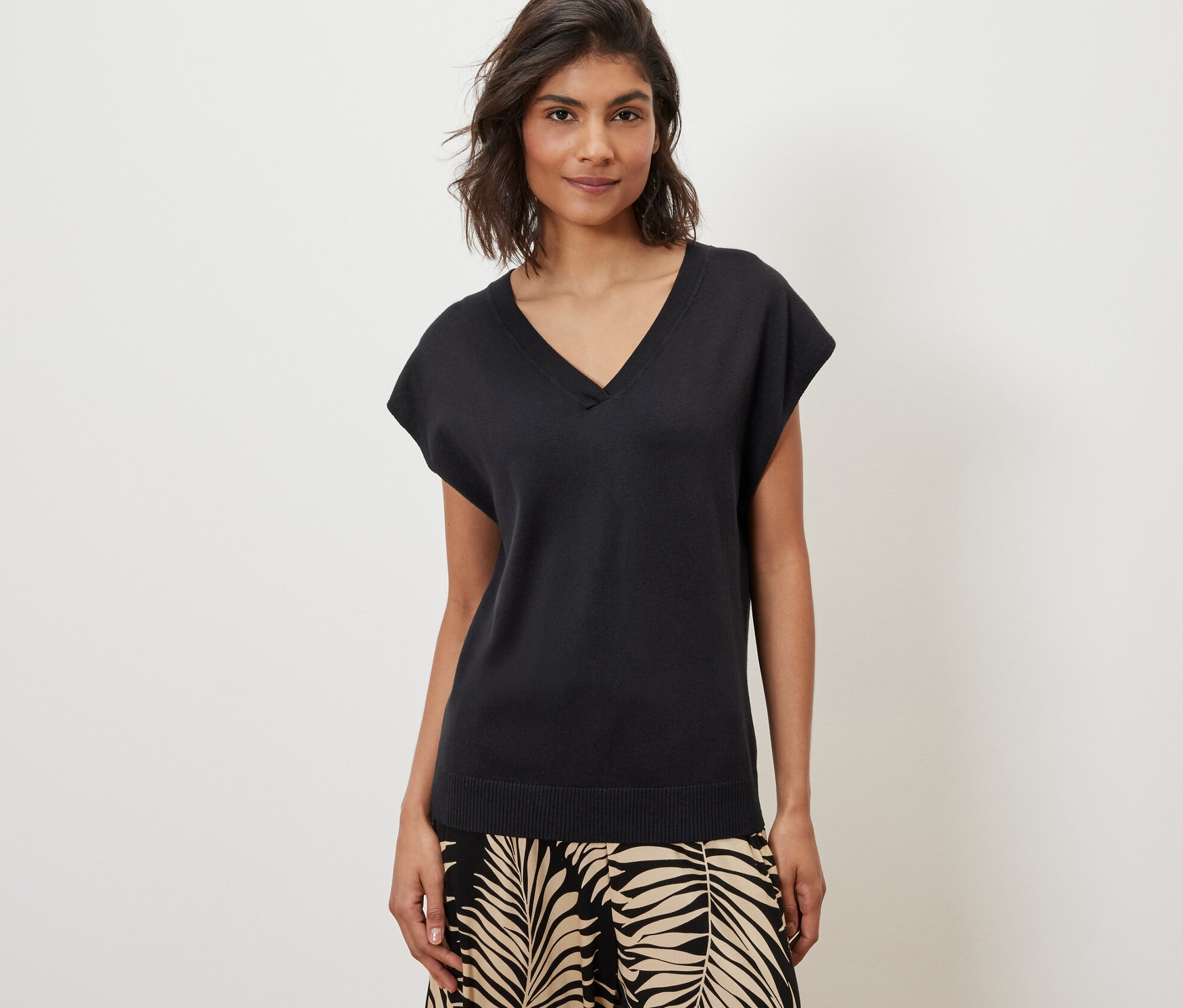 Frau trägt kurzärmligen Feinstrickpullover, schwarz, und gemusterte Hosen.