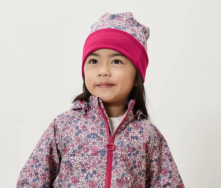 Lächelndes Mädchen trägt eine Blumenjacke und Mütze.