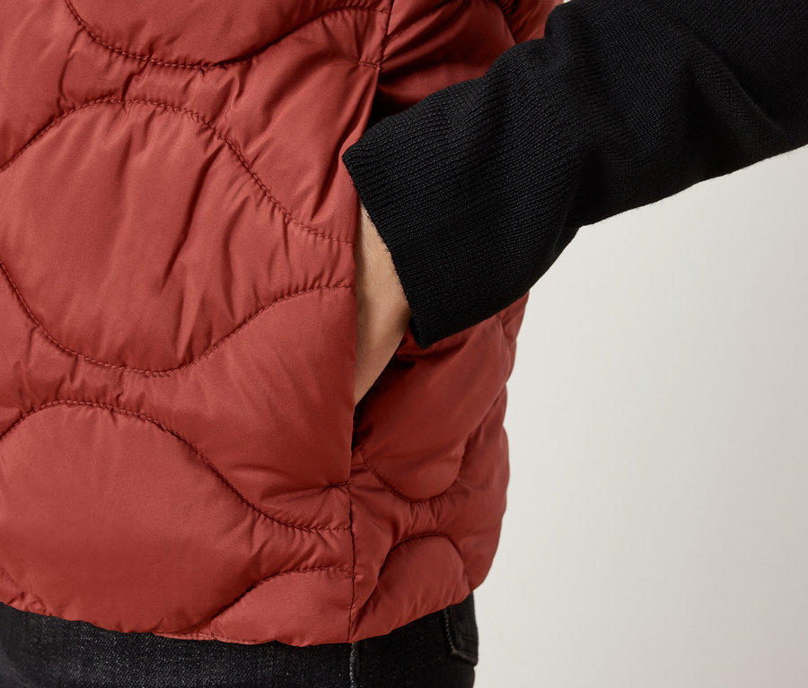 Detailaufnahme einer Person in einer braunen Steppweste mit der Hand in der Tasche.