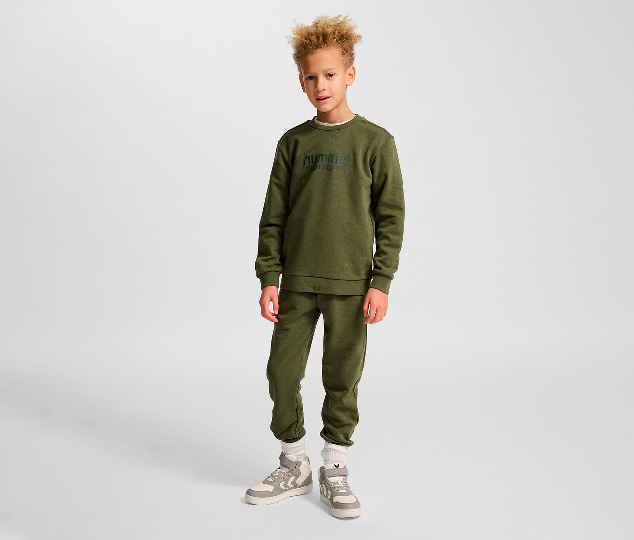 Junge steht in grünem HUMMEL HMLJR Base-Sweatshirt und Trainingshose.