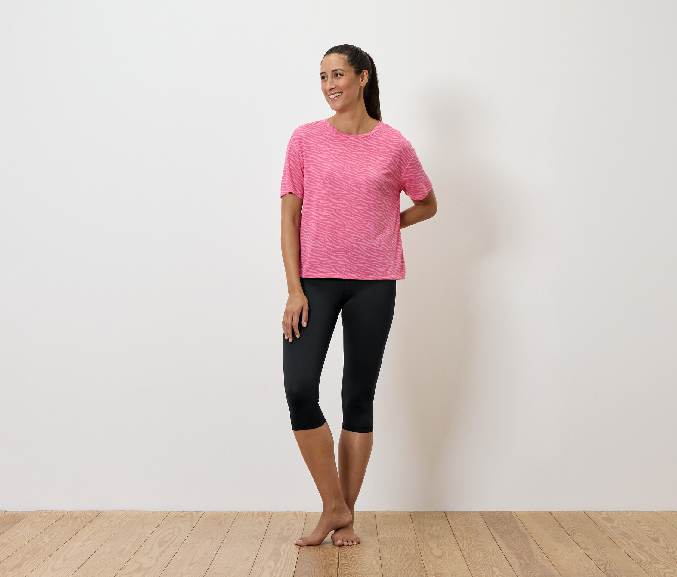 Eine Frau steht und trägt ein rosa T-Shirt und schwarze Leggings.