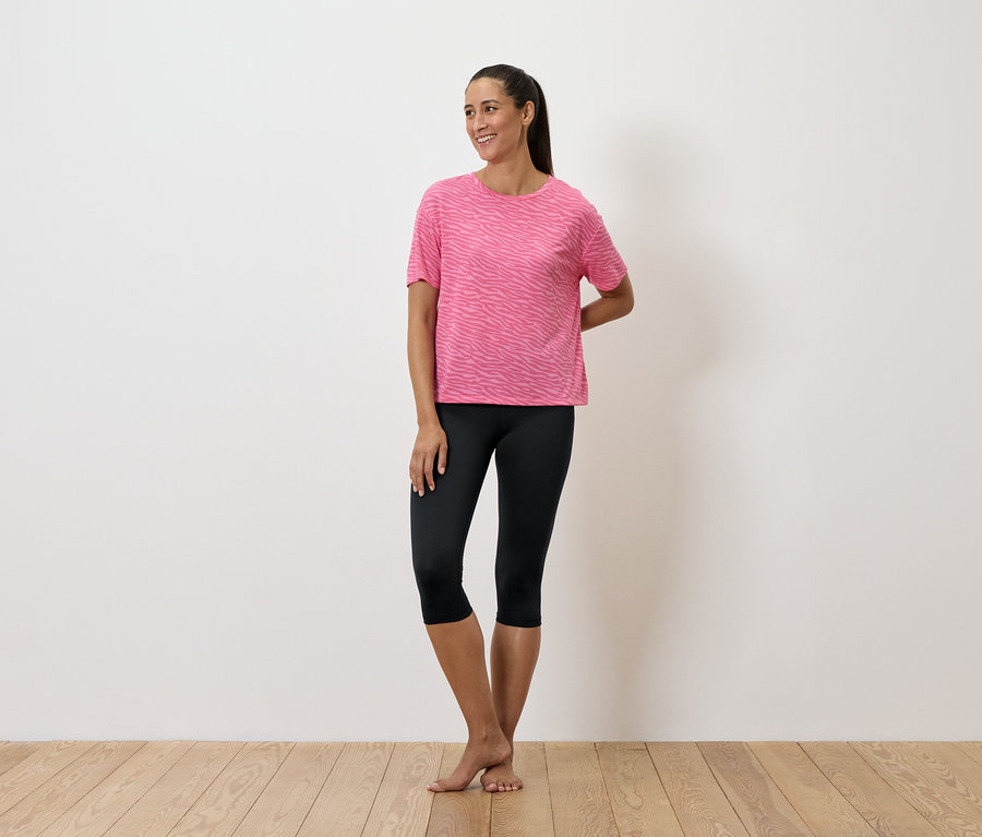 Eine Frau steht und trägt ein rosa T-Shirt und schwarze Leggings.