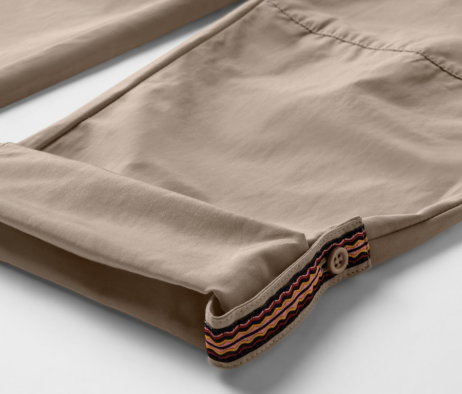 Detailaufnahme einer beigen Outdoorhose mit hochgekrempelten Hosenbeinen und dekorativer Borte mit Knopf. Die Hose hat einen Moskito-Schutz.