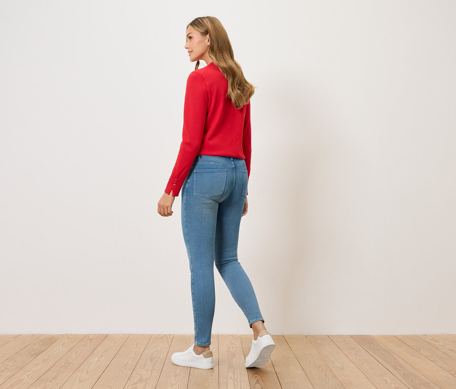 Frau geht, von hinten gesehen, mit rotem Pullover, blauen Jeans und weißen Turnschuhen.
