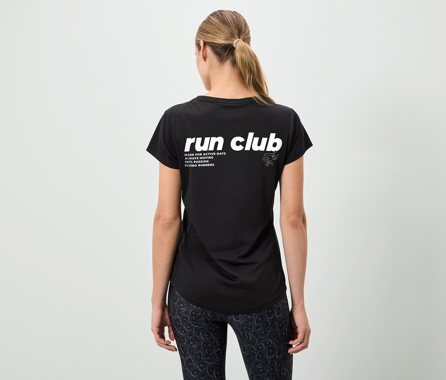Rückansicht einer Frau mit Pferdeschwanz in einem schwarzen T-Shirt mit der Aufschrift "run club" und gemusterten Leggings.