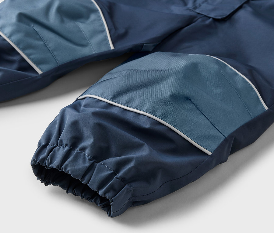 Nahaufnahme einer marineblauen Hose mit hellblauen Kniepatches und weißen Akzenten, die auf einer ebenen Fläche liegt.