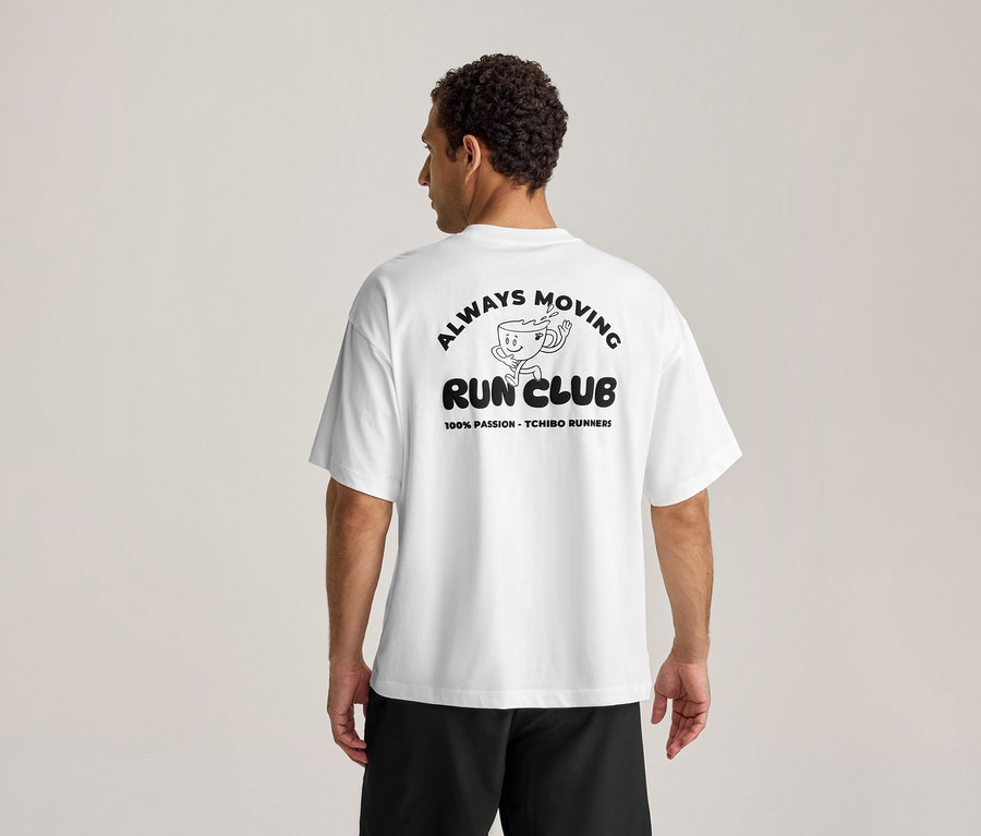 Mann von hinten in einem weißen Sportshirt mit schwarzem Aufdruck "ALWAYS MOVING RUN CLUB" und laufender Kaffeetasse.