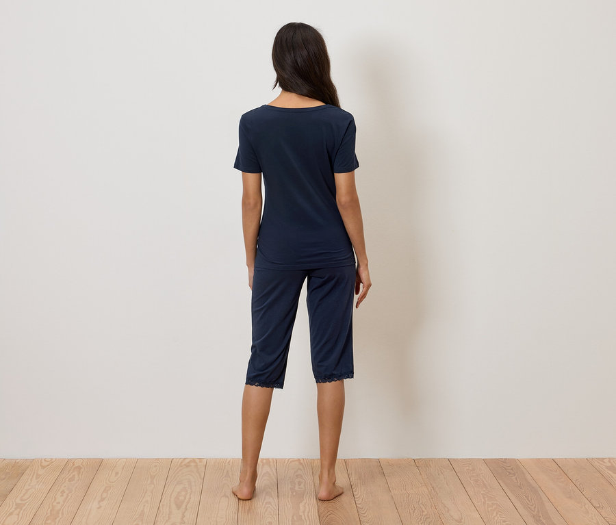 Eine Frau steht mit dem Rücken zur Kamera und trägt einen marineblauen Pyjama mit Spitzenbesatz.