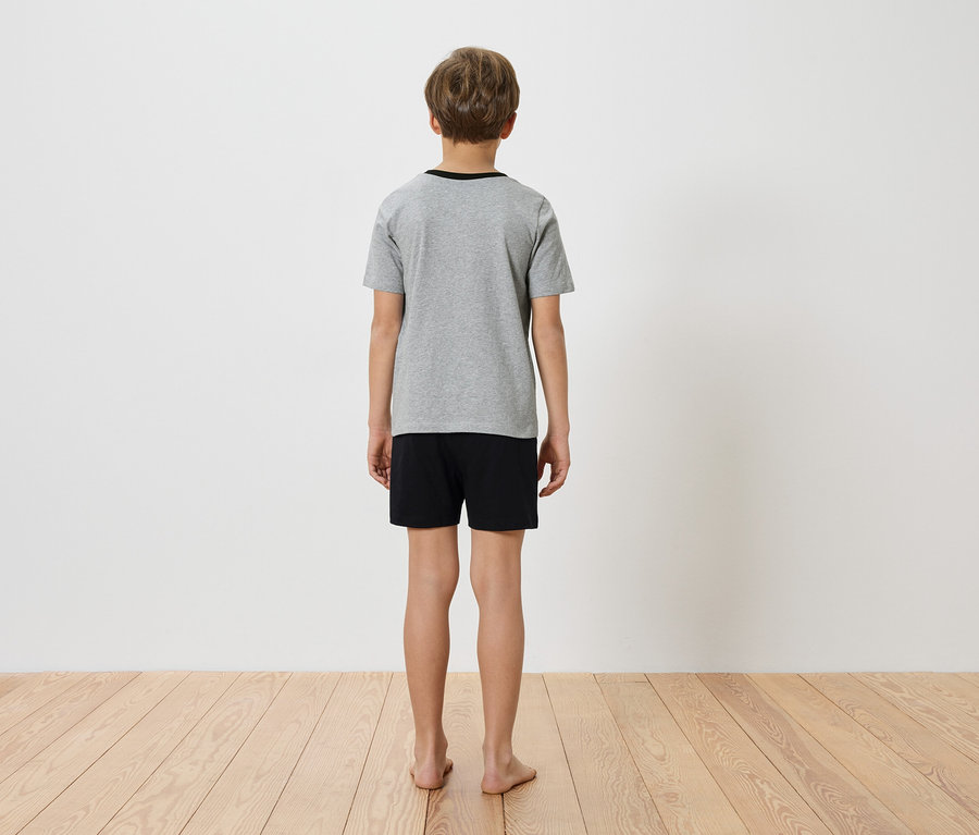Ein Kind steht mit dem Rücken zur Kamera, trägt ein graues T-Shirt und schwarze Shorts.