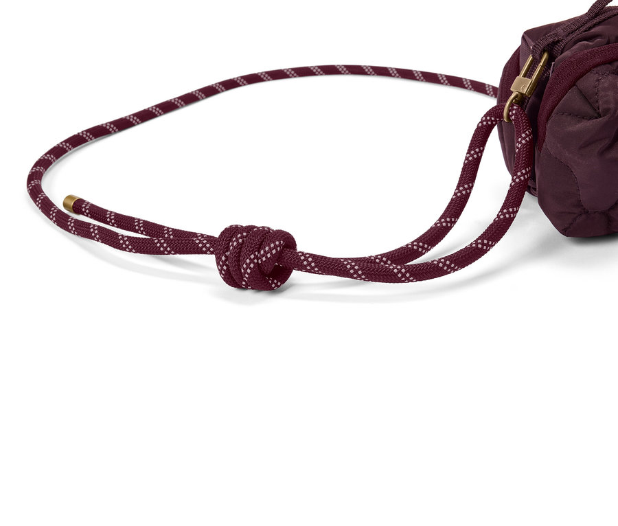 Nahaufnahme einer burgunderroten, gesteppten Tasche mit einem burgunderroten Kordelzug, der einen Knoten hat.