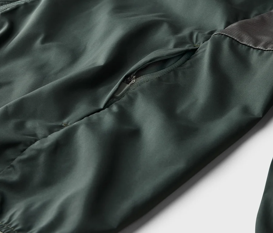 Nahaufnahme einer olivgrünen Jacke mit Reißverschlusstasche und grauem Mesh-Einsatz.