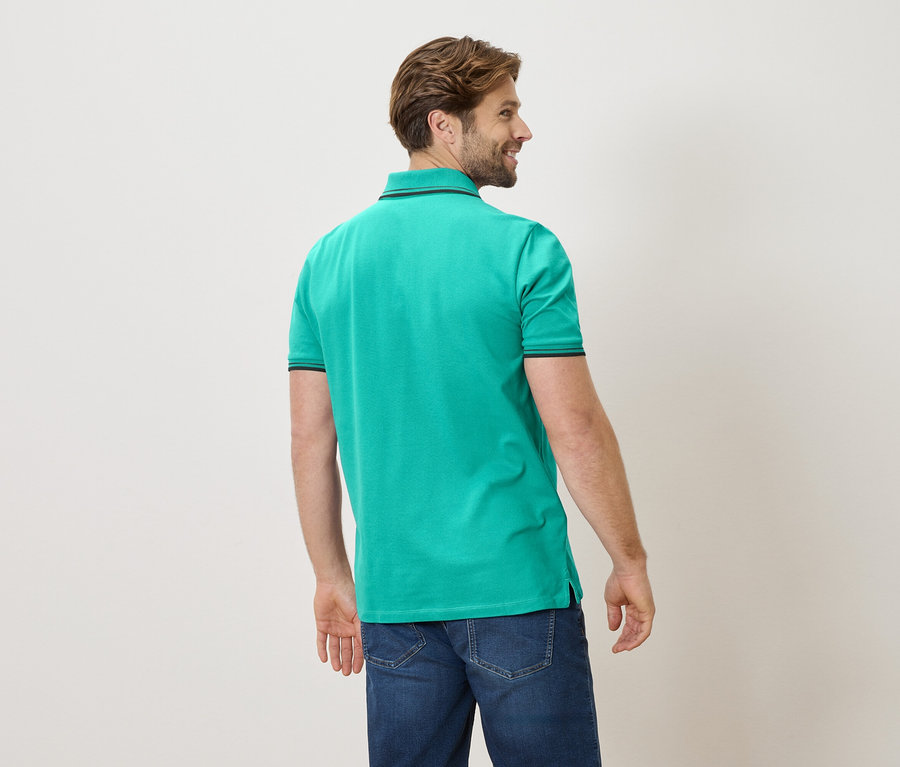 Ein Mann von hinten in einem grünen Poloshirt und Jeans.