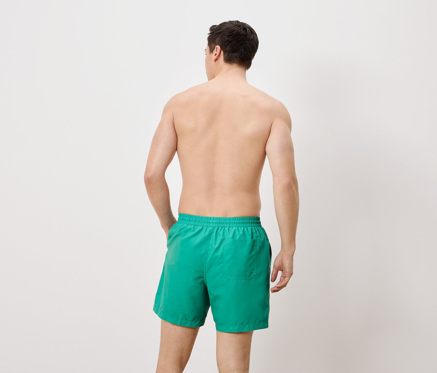 Ein Mann steht mit dem Rücken zur Kamera und trägt grüne Badeshorts.