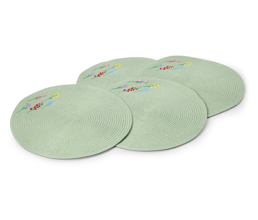 Vier runde, hellgrüne Tischsets mit gestickten Blumenmustern liegen übereinander.
