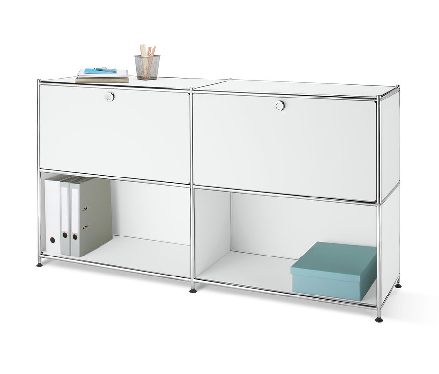 Frontansicht eines Metall-Sideboards mit 2 versetzbaren Klappenfächern, auf dem ein Notizbuch und ein Stiftehalter stehen. In einem offenen Fach befinden sich zwei Ordner und eine blaue Schachtel.