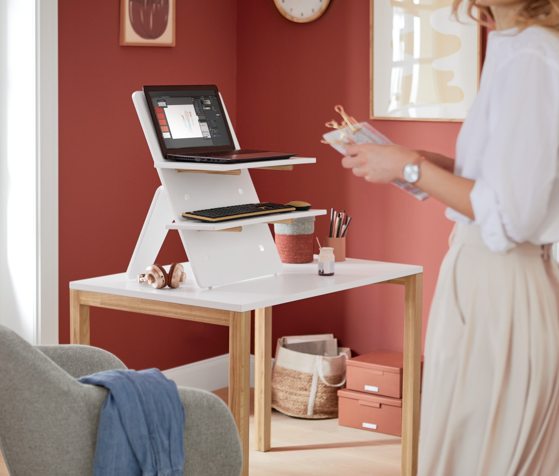 Eine Frau steht neben einem weißen Tisch mit einem weißen Schreibtischaufsatz, auf dem sich ein Laptop und eine Tastatur befinden.