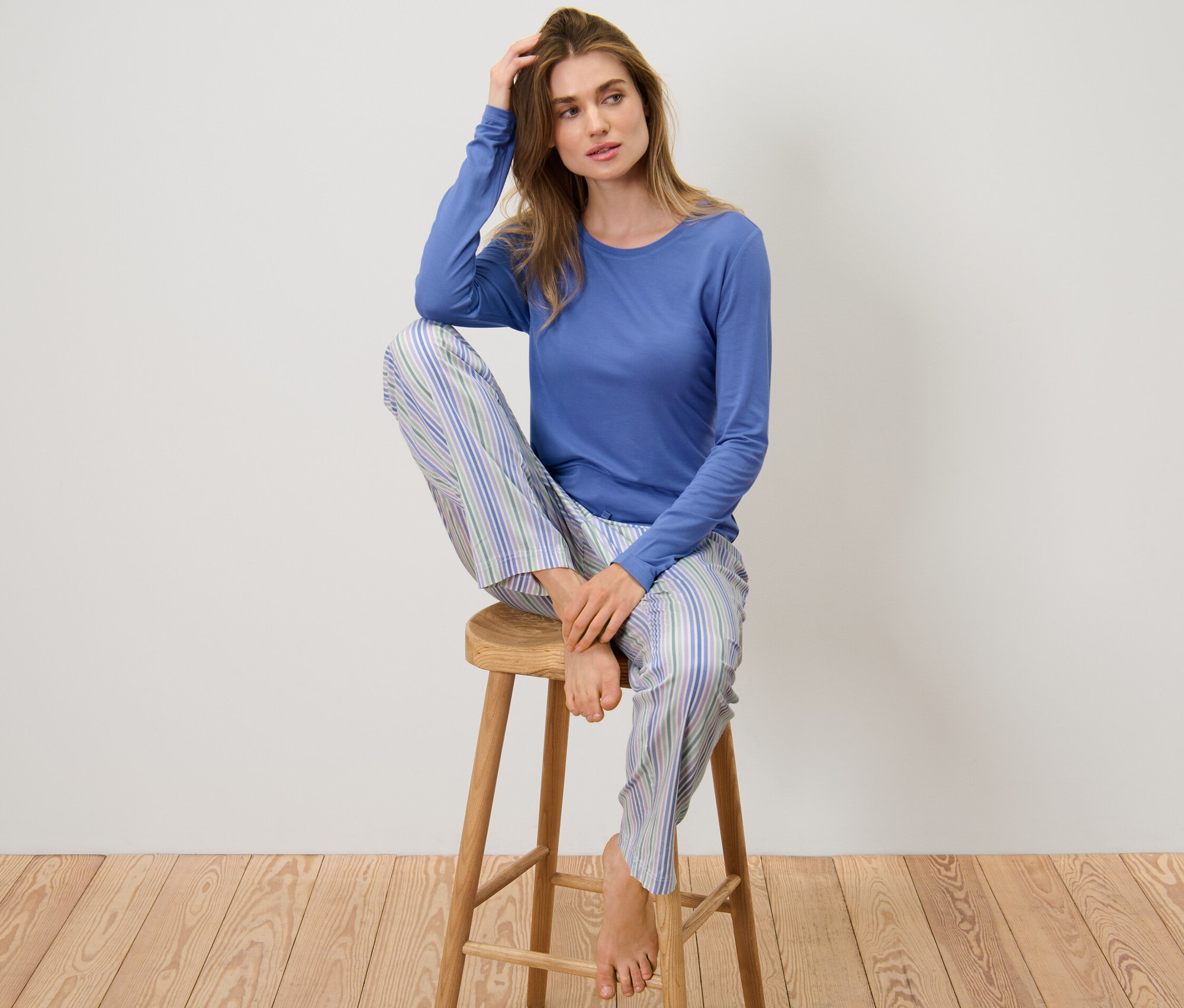 Frau sitzt in einem Pyjama mit Webhose auf einem Hocker.