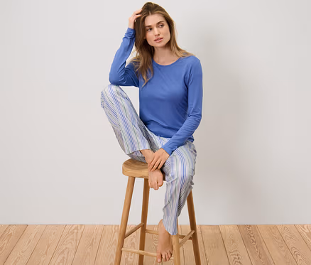 Frau sitzt in einem Pyjama mit Webhose auf einem Hocker.