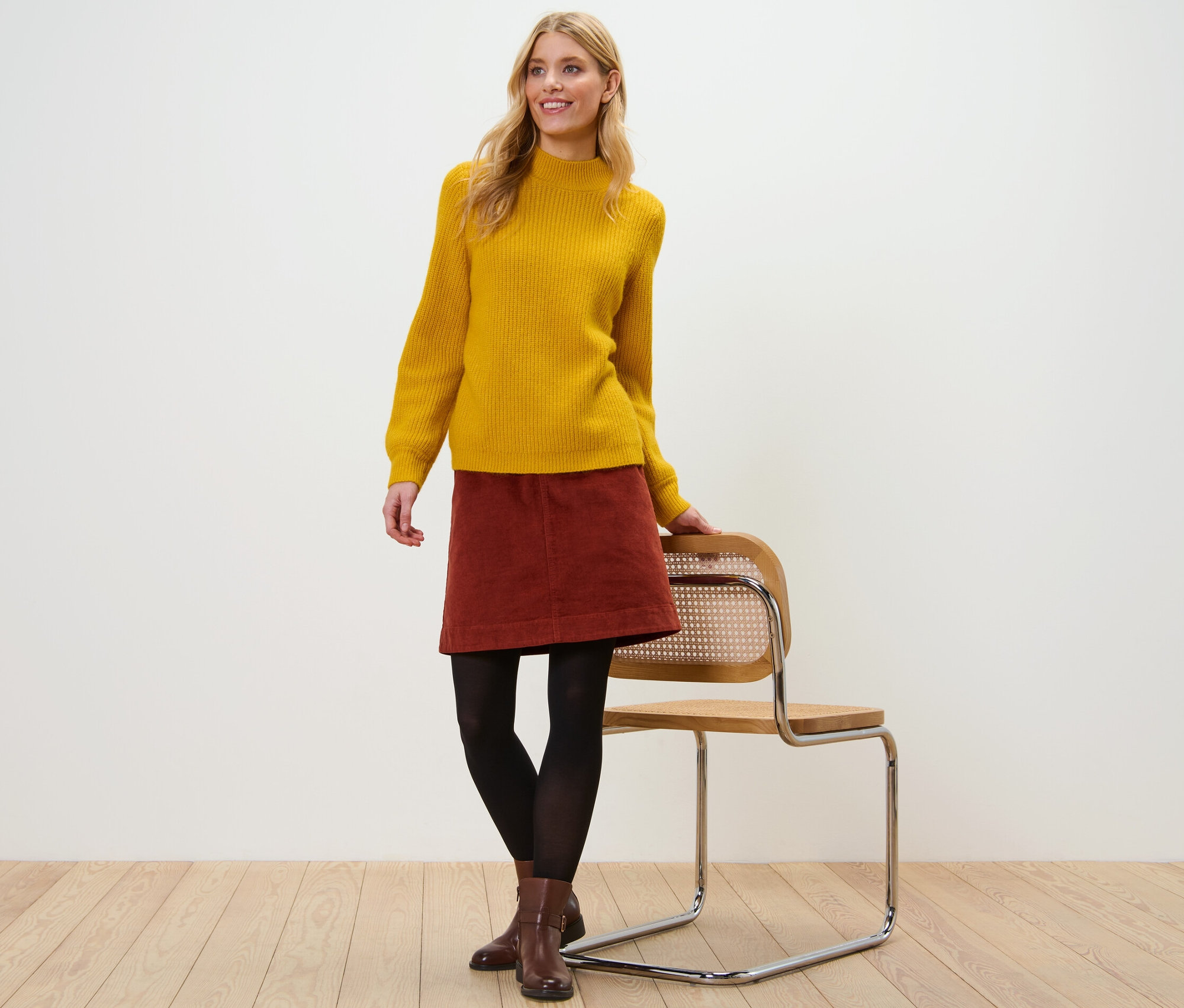 Frau posiert in gelbem Pullover und Cordrock.